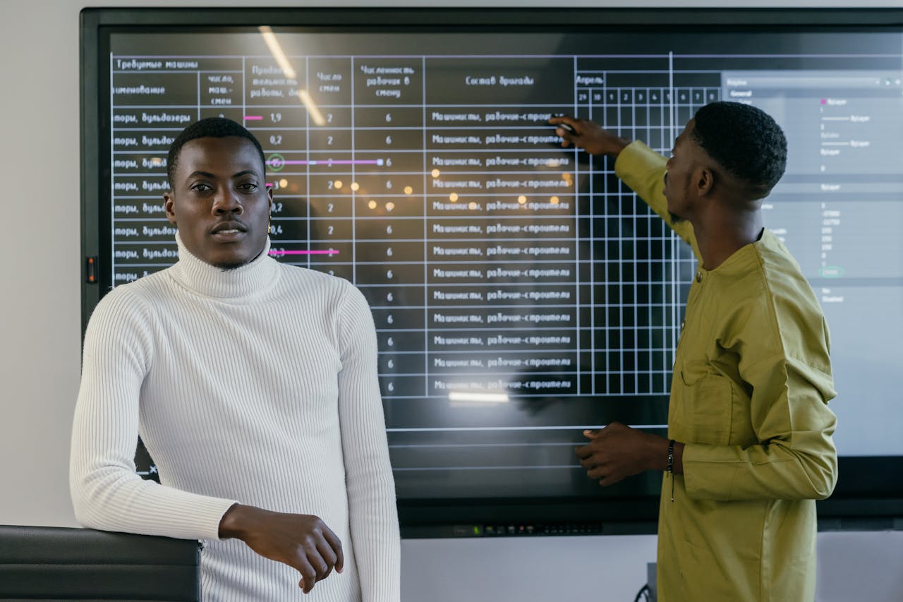 Two professionals collaborate in front of a large screen during a business meeting, focusing on teamwork and technology.