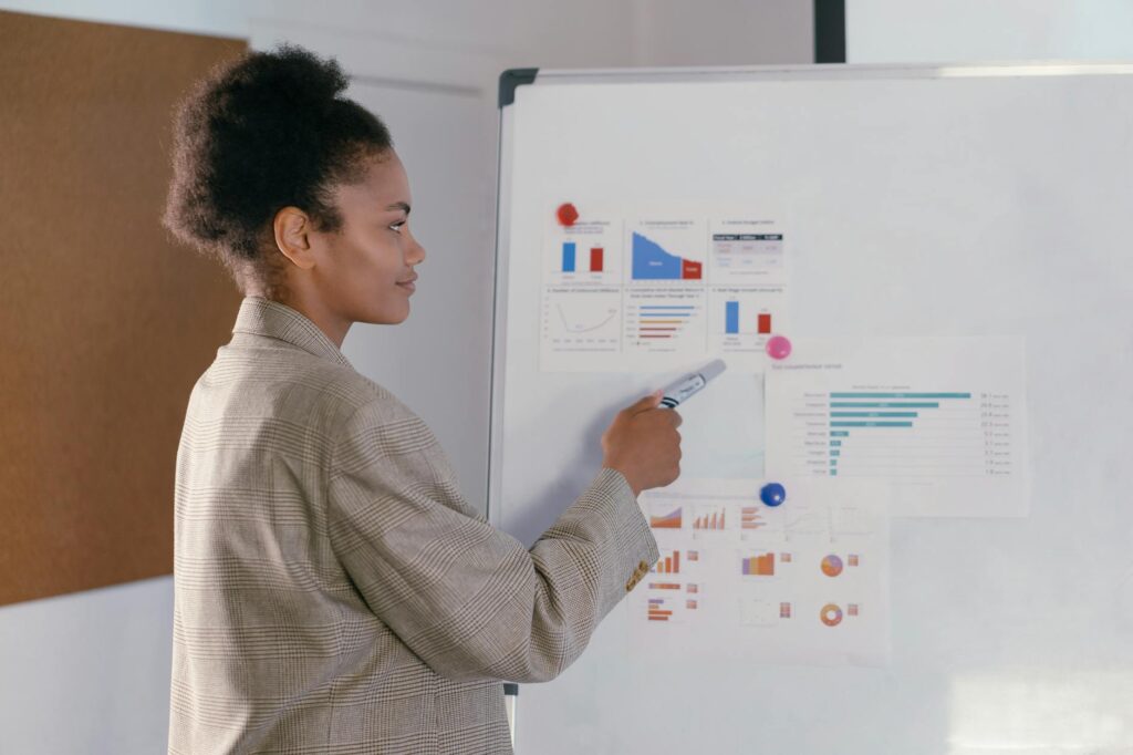 Professional woman in a blazer discusses finance graphs on a whiteboard during a presentation.